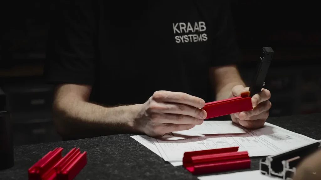 Инженер KRAAB SYSTEMS держит красный образец профиля